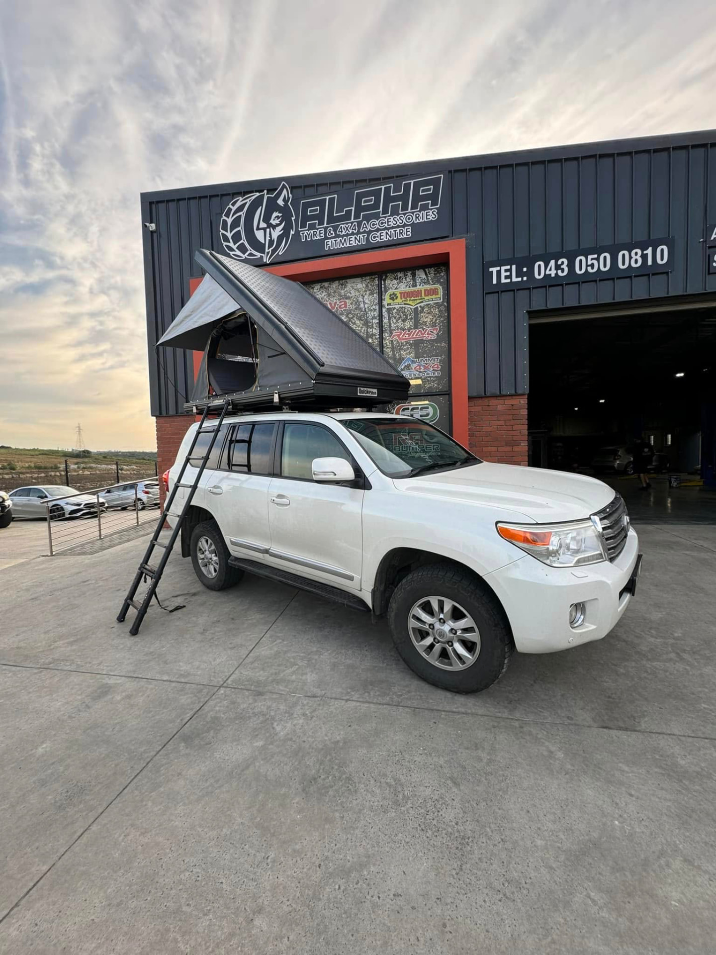 Toyota Land Cruiser 200 fitted with a QuickPitch rooftop tent and ladder outside the Alpha Tyre & 4x4 fitment centre in East London