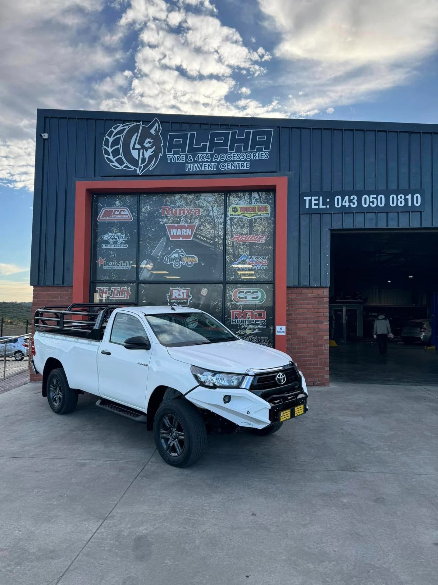 Toyota Hilux single-cab fitted with a bull bar, winch, side steps, alloy wheels and a bed rack outside the Alpha Tyre & 4x4 fitment centre in East London