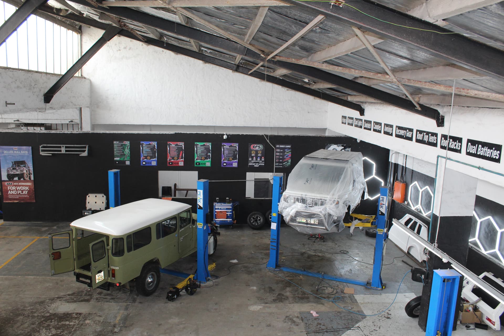 Classic Land Cruiser and Suzuki Jimny up on the Peak two-post lifts inside the Alpha workshop